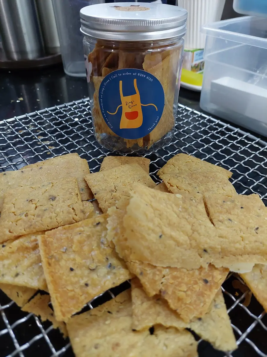 Thin sourdough crackers cooling on a rack beside a jar of them